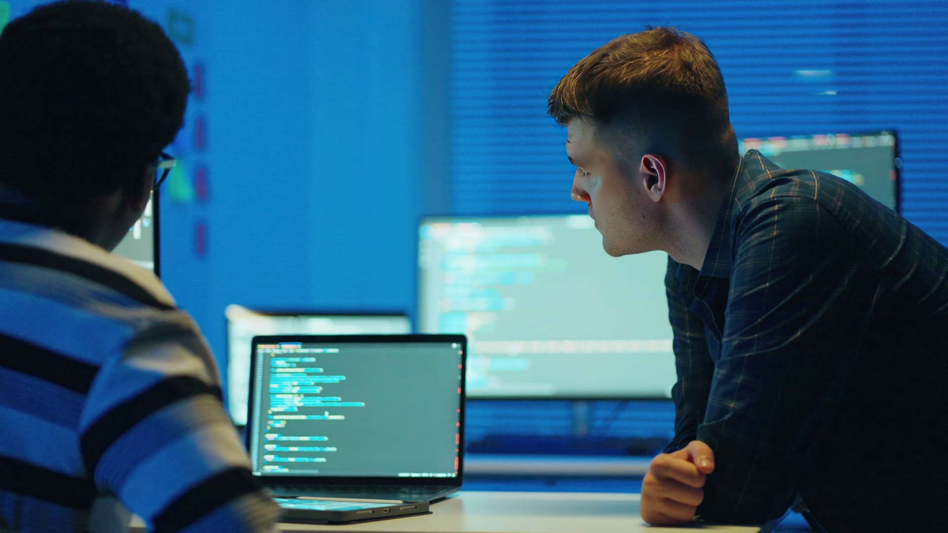 Improve automated workflows and streamline Software testing with nachine learning in software development. Software engineer discussed with software developer coding or debugging code on a laptop with multiple scree  at his desk in the tech office.